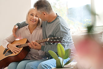 Senior couple playing acoustic guitar together on sofa