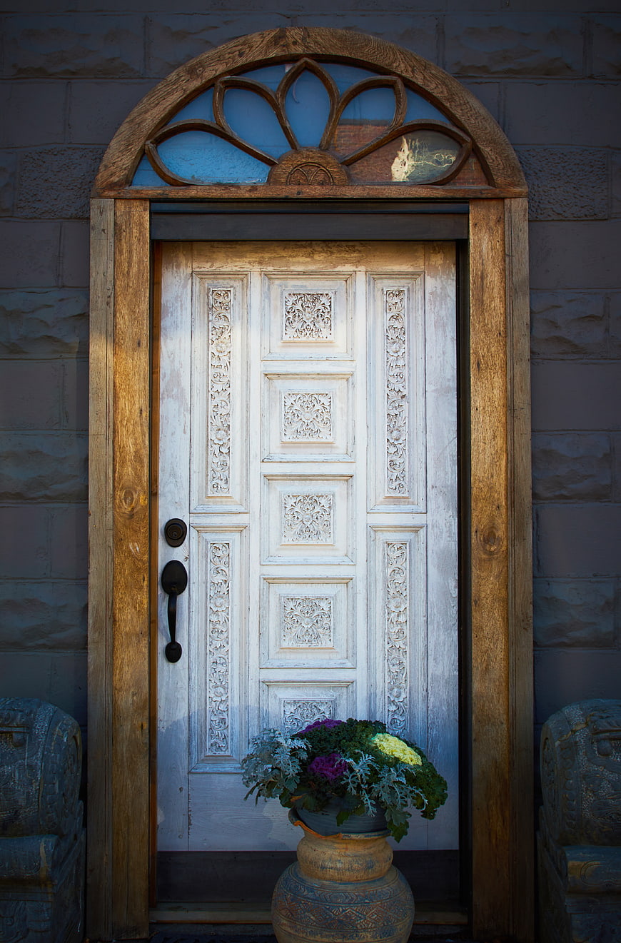 Weathered White Wooden Door with Carved Details and Floral Arrangement