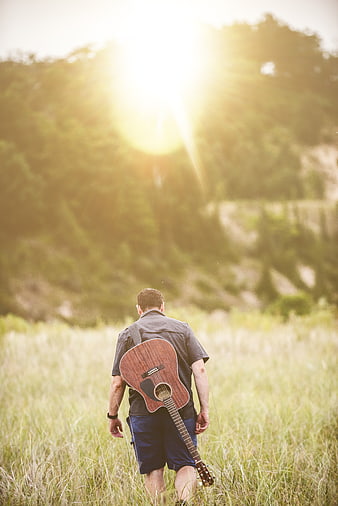 Man with Guitar Walking in Grassy Field at Sunset