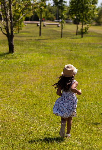 Little girl running in grassy field wearing straw hat