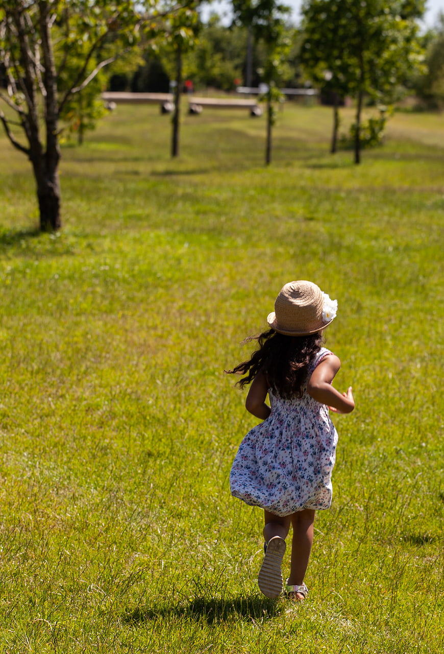 Little girl running in grassy field wearing straw hat