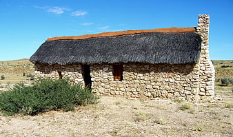 Rustic stone cottage with thatched roof in arid landscape