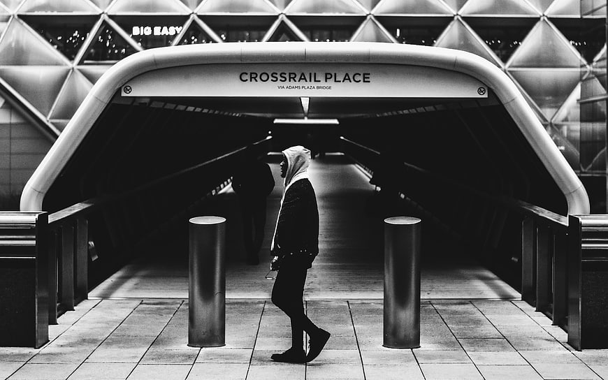 Black and white photo of person walking through Crossrail Place tunnel