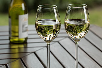 Two glasses of white wine on a wooden table outdoors