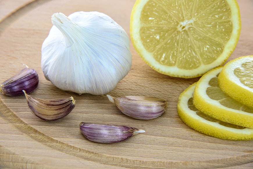 Fresh garlic bulb and sliced lemon on wooden board