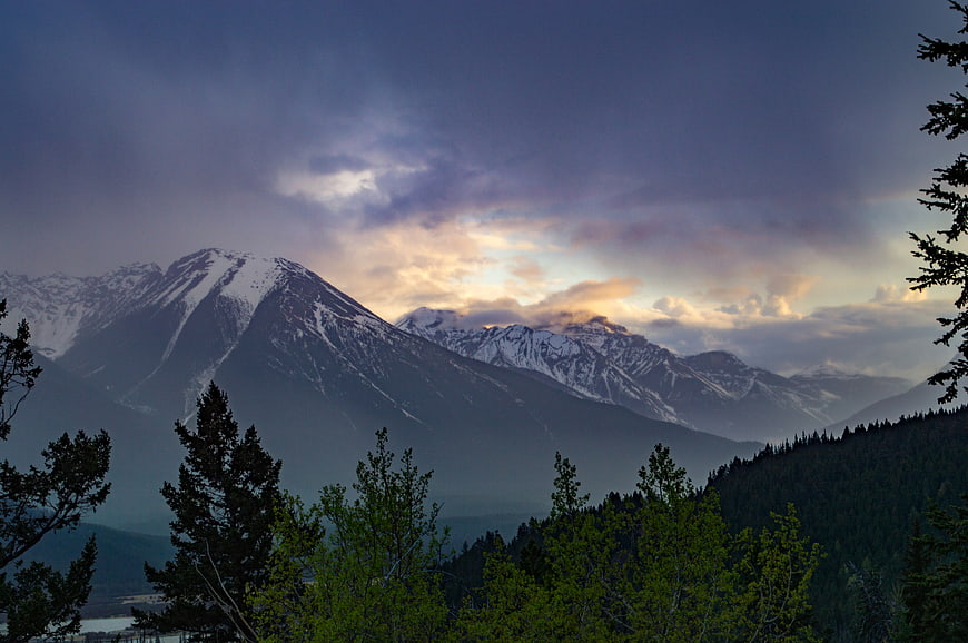 Dramatic Snow-Capped Mountain Range at Sunset with Foreground Trees