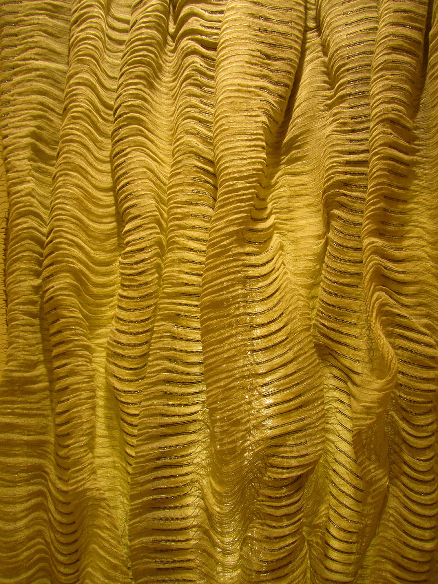 Golden pleated fabric texture with shiny metallic folds and abstract pattern