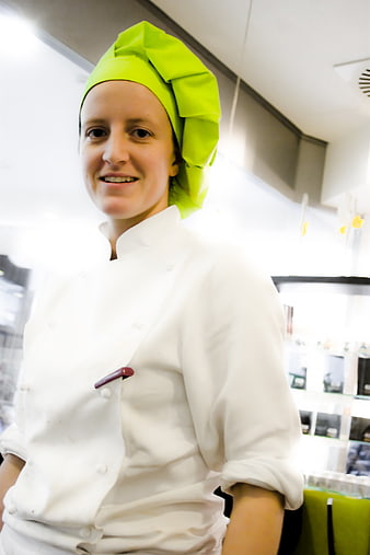 Smiling female pastry chef in white uniform and green hat