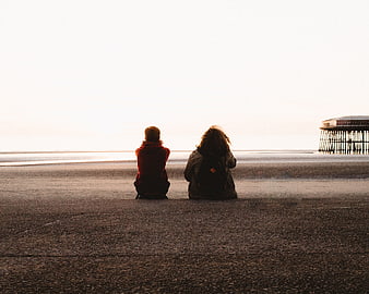 Couple sitting on beach looking at pier at sunset