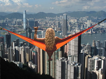 Woman relaxing in orange hammock with Hong Kong skyline view