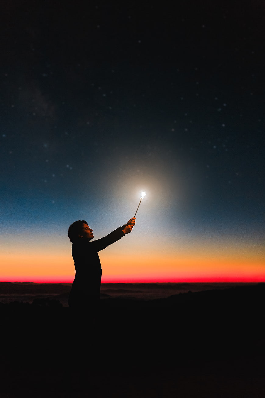Silhouette of Woman Holding Sparkler Against Starry Night Sky