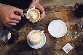 Barista pouring latte art into cappuccino cup top view