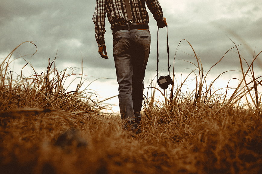 Photographer Walking Through Tall Grass with Camera