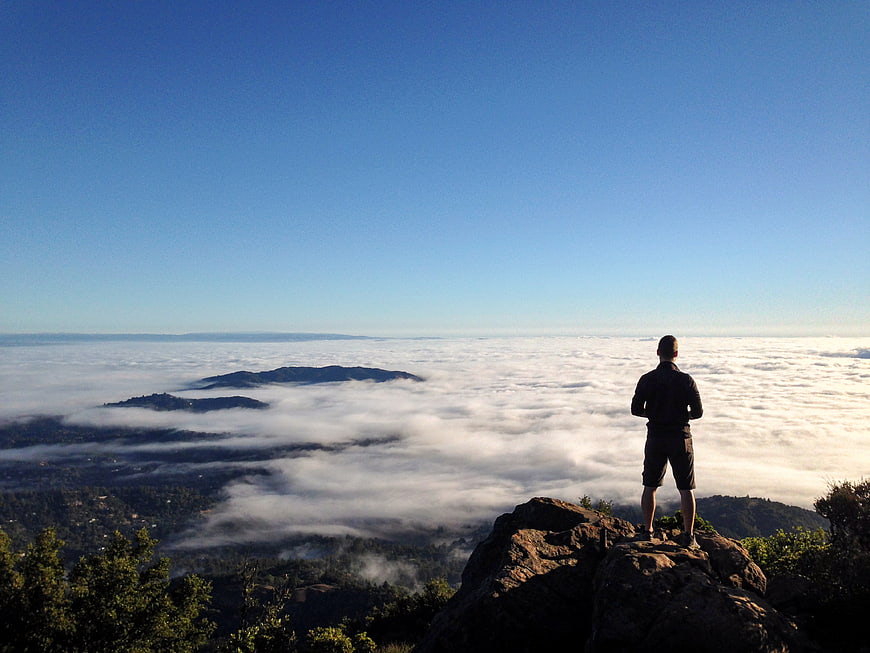 Man Standing on Rocky Peak Above Sea of Clouds