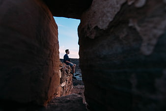 Man sitting on cliff edge framed by dark rocks