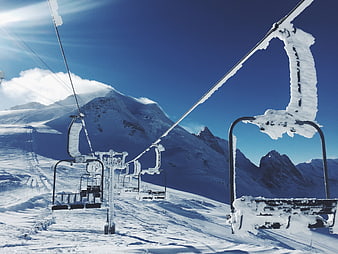 Snow-covered chairlift in alpine mountains under blue sky