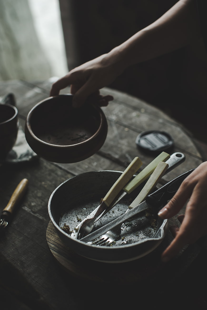 Hands clearing dirty dishes from rustic wooden table
