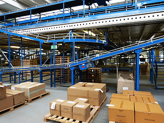 Interior of a large logistics warehouse with blue conveyor systems and cardboard boxes