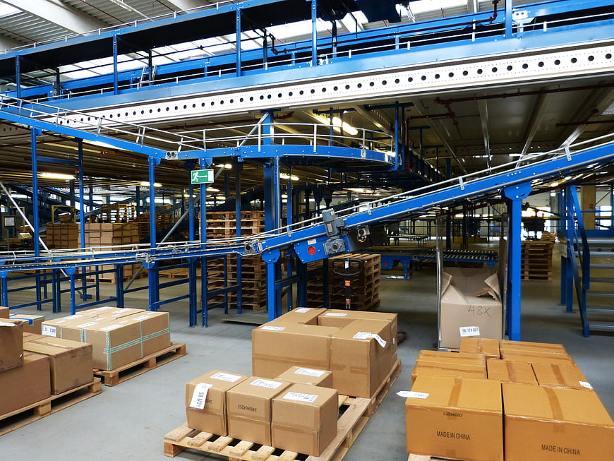 Interior of a large logistics warehouse with blue conveyor systems and cardboard boxes