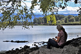 Woman sitting on rocks by a lake using smartphone in nature