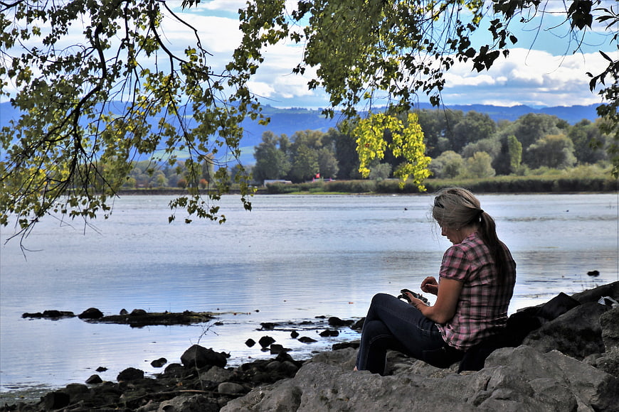 Woman sitting on rocks by a lake using smartphone in nature