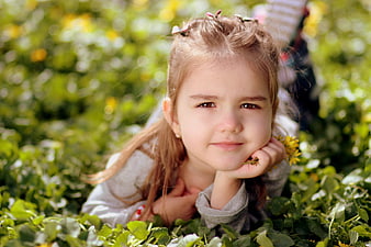 Cute little girl lying in green clover field with yellow flowers