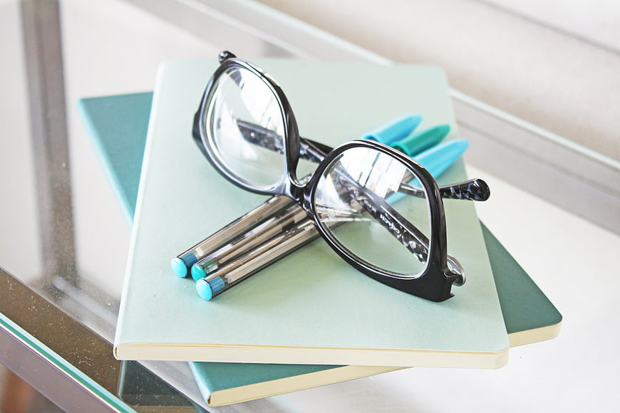 Black Reading Glasses on Mint Notebook with Blue Pens