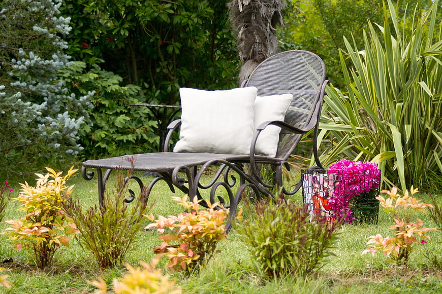 Wrought iron garden chaise lounge with white pillows and pink flowers