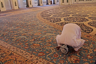 Muslim man praying in prostration on ornate mosque carpet
