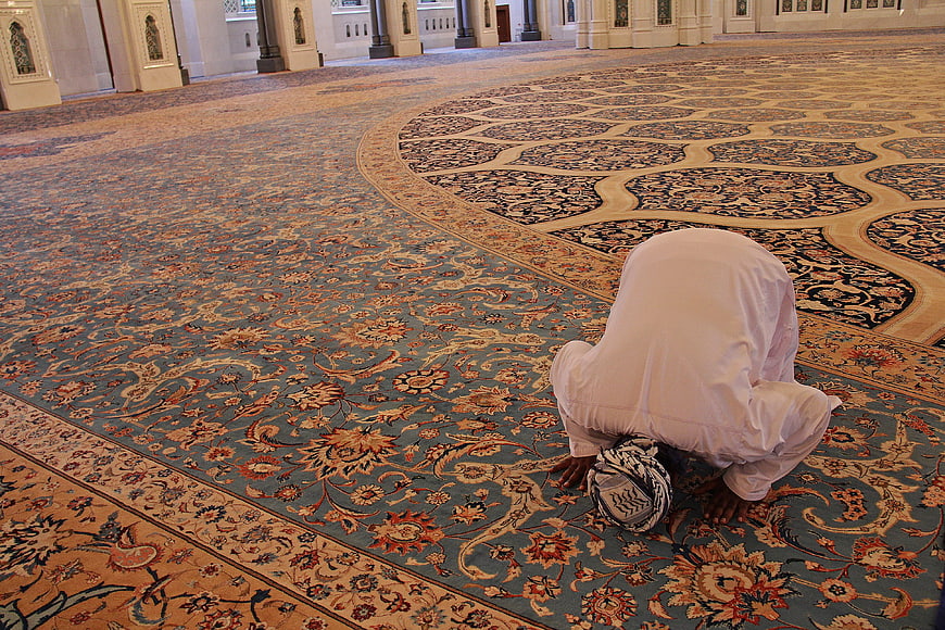 Muslim man praying in prostration on ornate mosque carpet