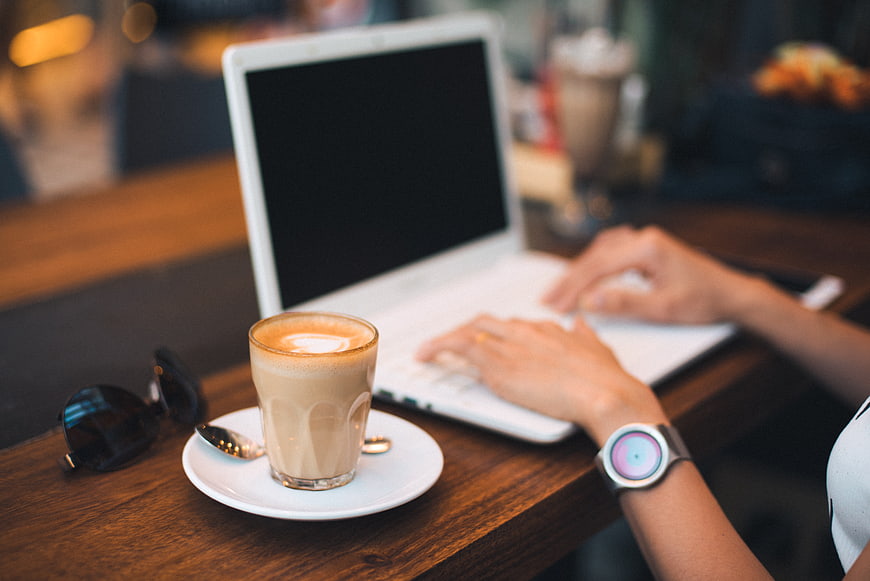 Person typing on laptop with coffee in cafe