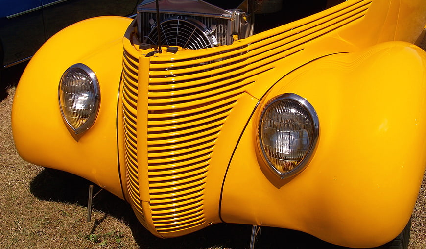 Close-up of a vintage yellow hot rod front grille and headlights