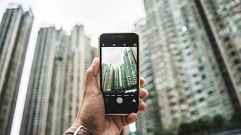 Hand holding smartphone photographing city skyscrapers