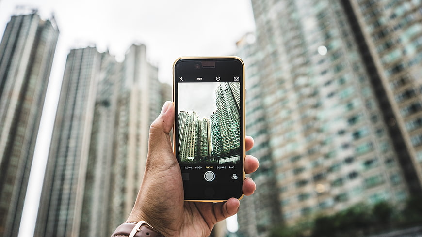 Hand holding smartphone photographing city skyscrapers