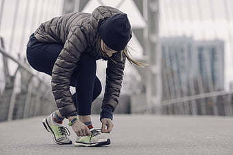 Woman tying running shoes on bridge in winter