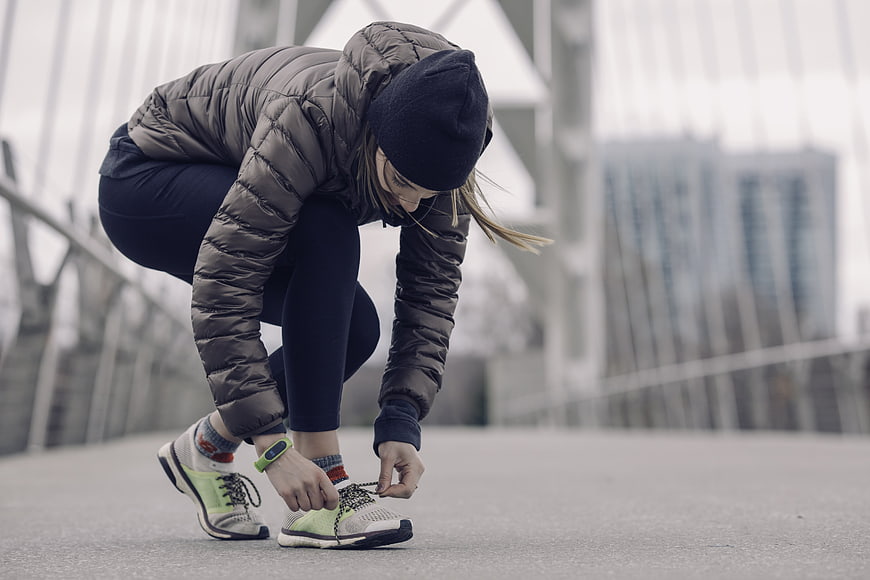 Woman tying running shoes on bridge in winter