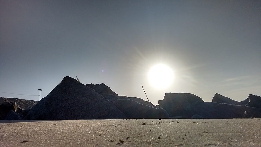 Low angle view of rocky beach with bright sun flare