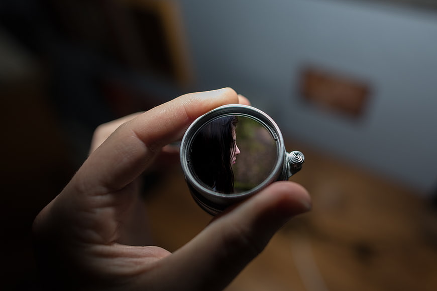 Hand holding small round mirror reflecting woman's profile