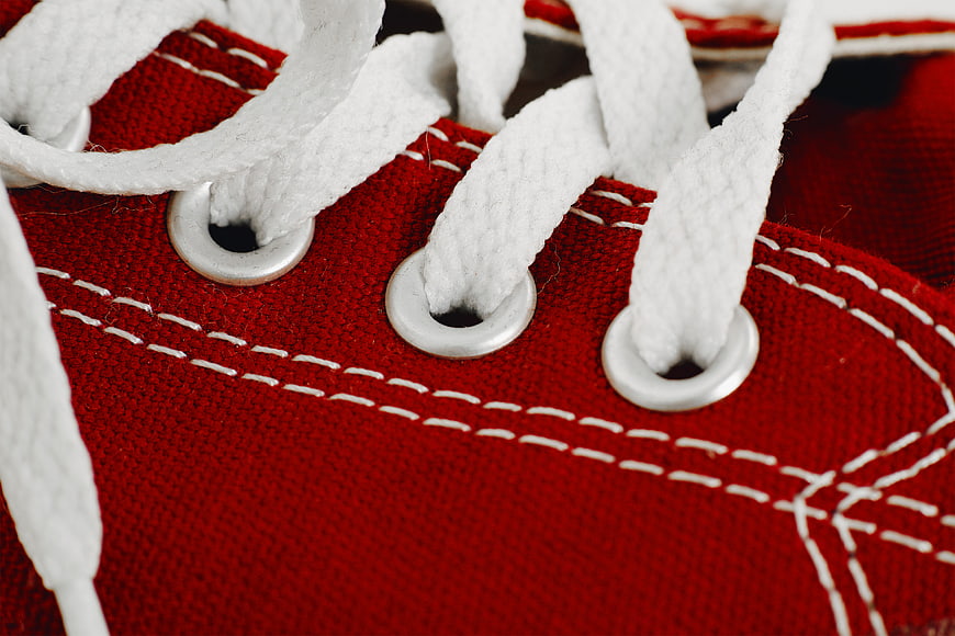 Close-up of red canvas shoe with white laces and stitching