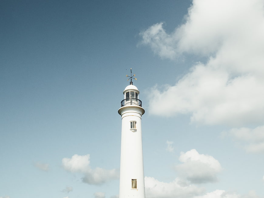 White Lighthouse Tower Against Blue Sky with Clouds