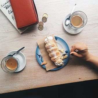 Top view of hand eating pastry with espresso on wooden table