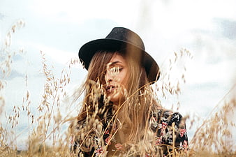 Woman in black hat standing in tall dry grass field
