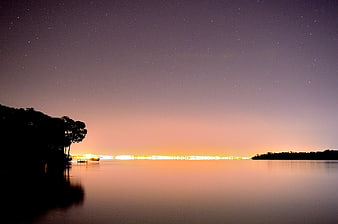 Serene Night Sky Over Calm Water with Distant City Lights