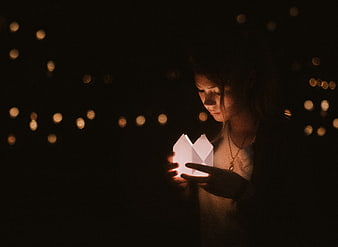 Woman holding glowing paper lantern at night with bokeh lights