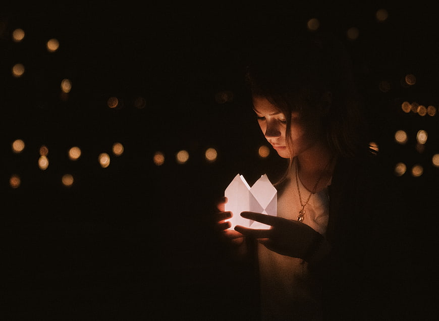 Woman holding glowing paper lantern at night with bokeh lights