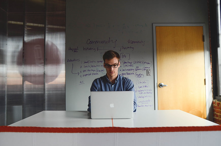 Young man working on laptop in modern office with whiteboard