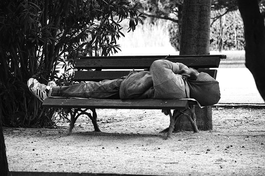 Black and white photo of person sleeping on park bench