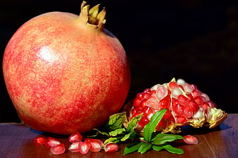 Fresh Pomegranate With Exposed Seeds And Green Leaves On Wooden Surface