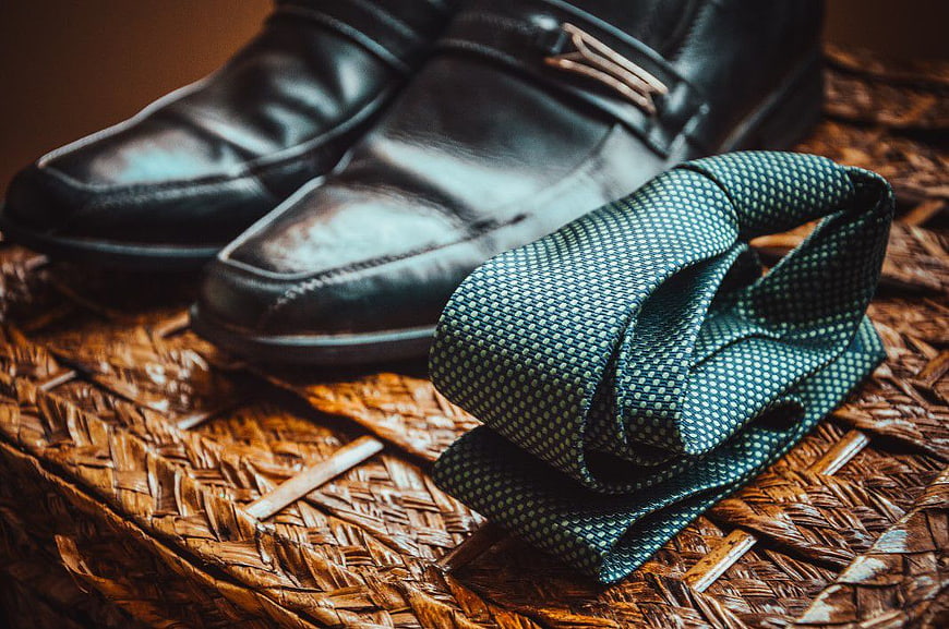 Black leather loafers and patterned tie on woven mat