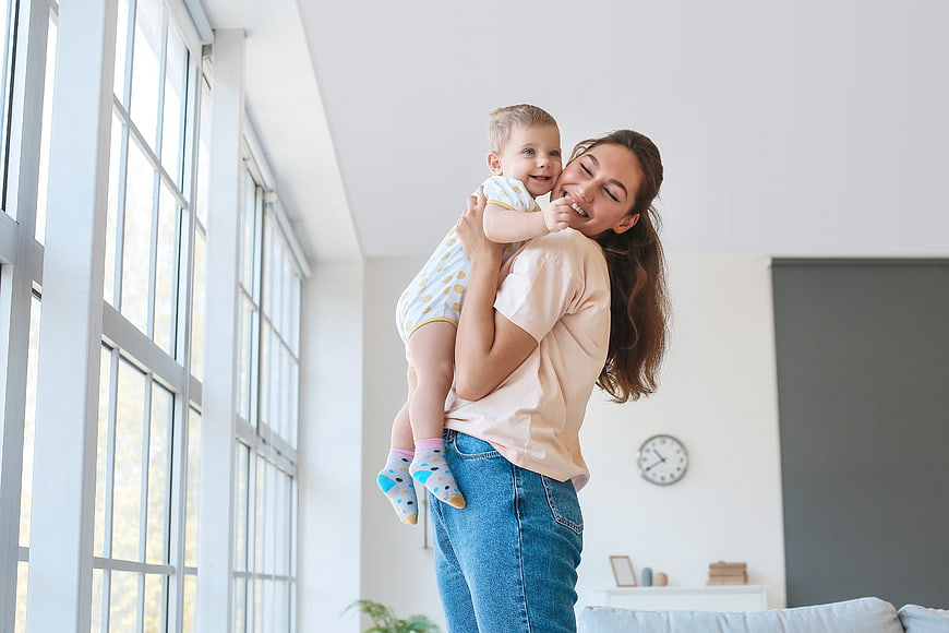 Happy Mother Holding Toddler Boy in Bright Living Room